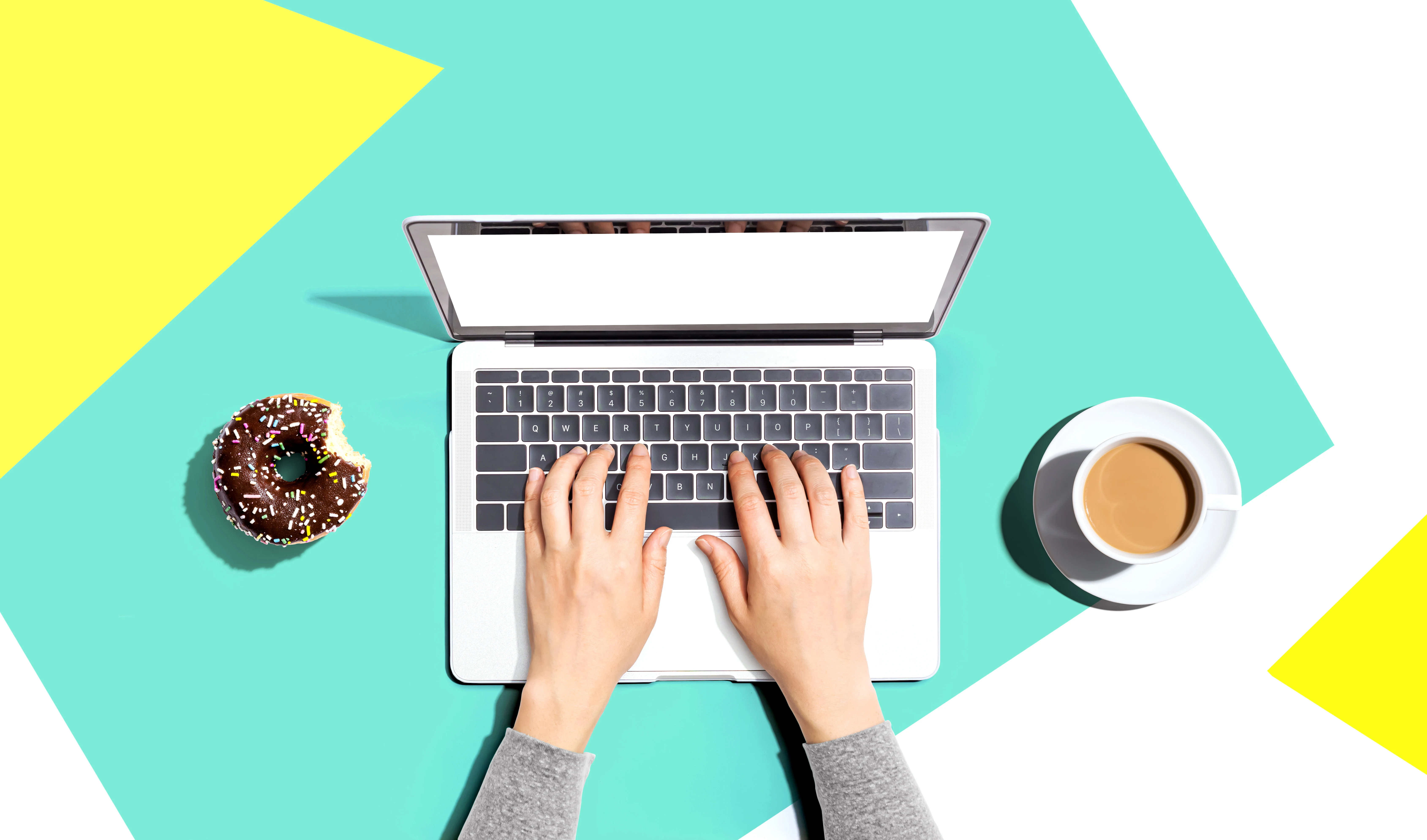 Pessoa usando um laptop com um donut e uma xícara de café - Flat lay