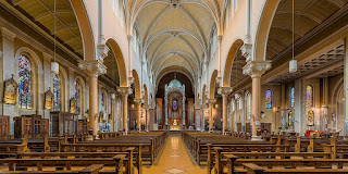 Interior view of the white arches, goldtone pews and stained glass windows of Whitefriar Street Church in Dublin, Ireland