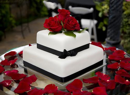 Two tier white square cake with black ribbons around tiers and red roses on