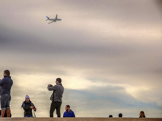 Gente tomando fotografías y sobre ellos avión volando en las alturas