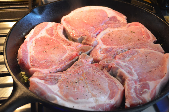Uncooked Pork Chops seasoned with salt and pepper in a cast iron pan.