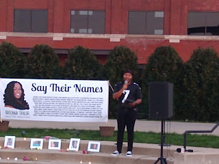 speaker with microphone, "Say Their Names" poster