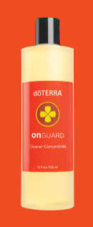 Close-up of the dōTERRA On Guard Cleaner Concentrate bottle. The label is prominently displayed, showing the On Guard logo and essential information. The bottle is positioned on a pristine white background, highlighting its bright orange cap.