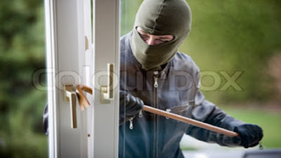Hooded burgler trying to break into a house with a crowbar.