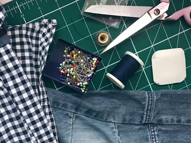 A picture of cutting board with scissors, thread, tailors chalk, pins and a shirt and trousers laid out on it