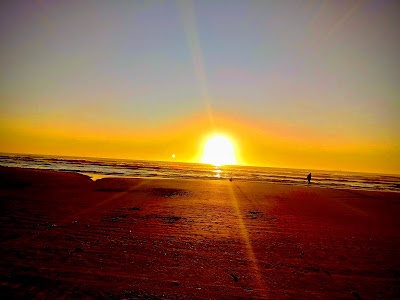 A foto mostra o sol nascendo radiante sobre as águas da praia. Geralmente muitos pais e filhos aproveitam as férias em viagens e lindas praias do Brasil e do mundo. Outros se divertem com outras maneiras e de acordo com as possibilidades financeiras. 