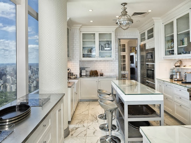 Kitchen in a NYC penthouse with marble floor, windows with a view of central park, subway tile backsplash, kitchen island with counter seating and glass upper cabinets