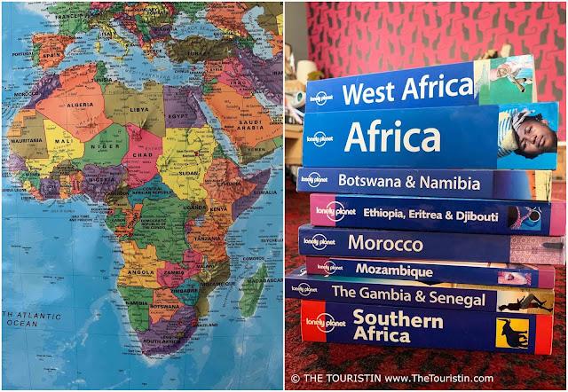 The map of Africa next to a stack of African travel guide books in front of a magenta coloured wallpaper featuring black cats.