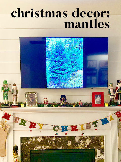 Fireplace mantle decorated with nutcrackers and greenery and a TV showing two christmas trees.