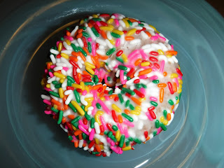 a donut with white frosting and rainbow sprinkles sits on a teal glass plate at Jitters Donuts in Sioux City, Iowa