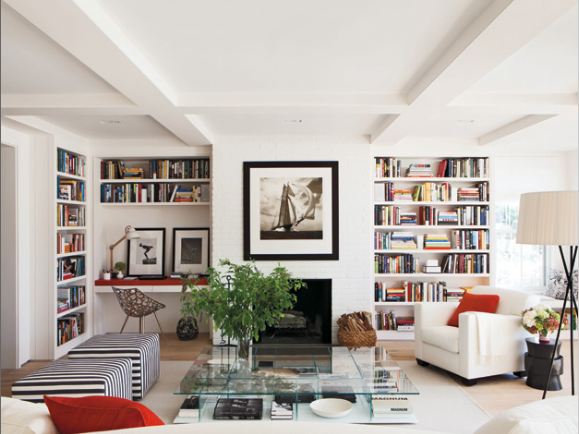 elle decor's nantucket retreat with a white living room, built in book shelves, striped ottomans and glass coffeetable