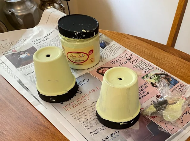 Photo of terracotta pots getting painted with green paint.