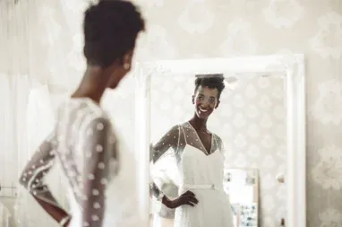 A lady wearing a white dress looks into a mirror