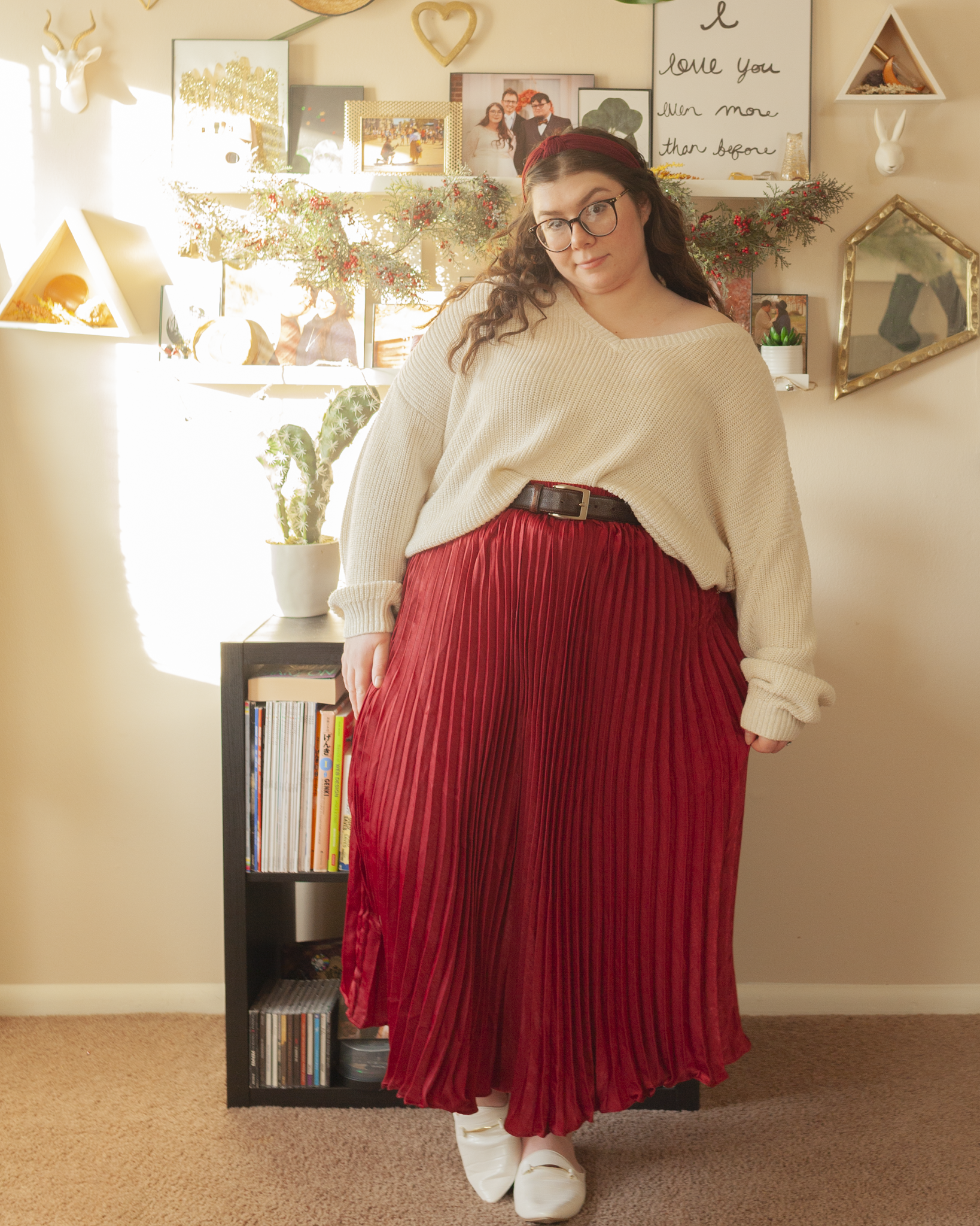 An outfit consisting of an oversized white v-neck sweater with gold threading half tucked into a wine colored pleated midi skirt.