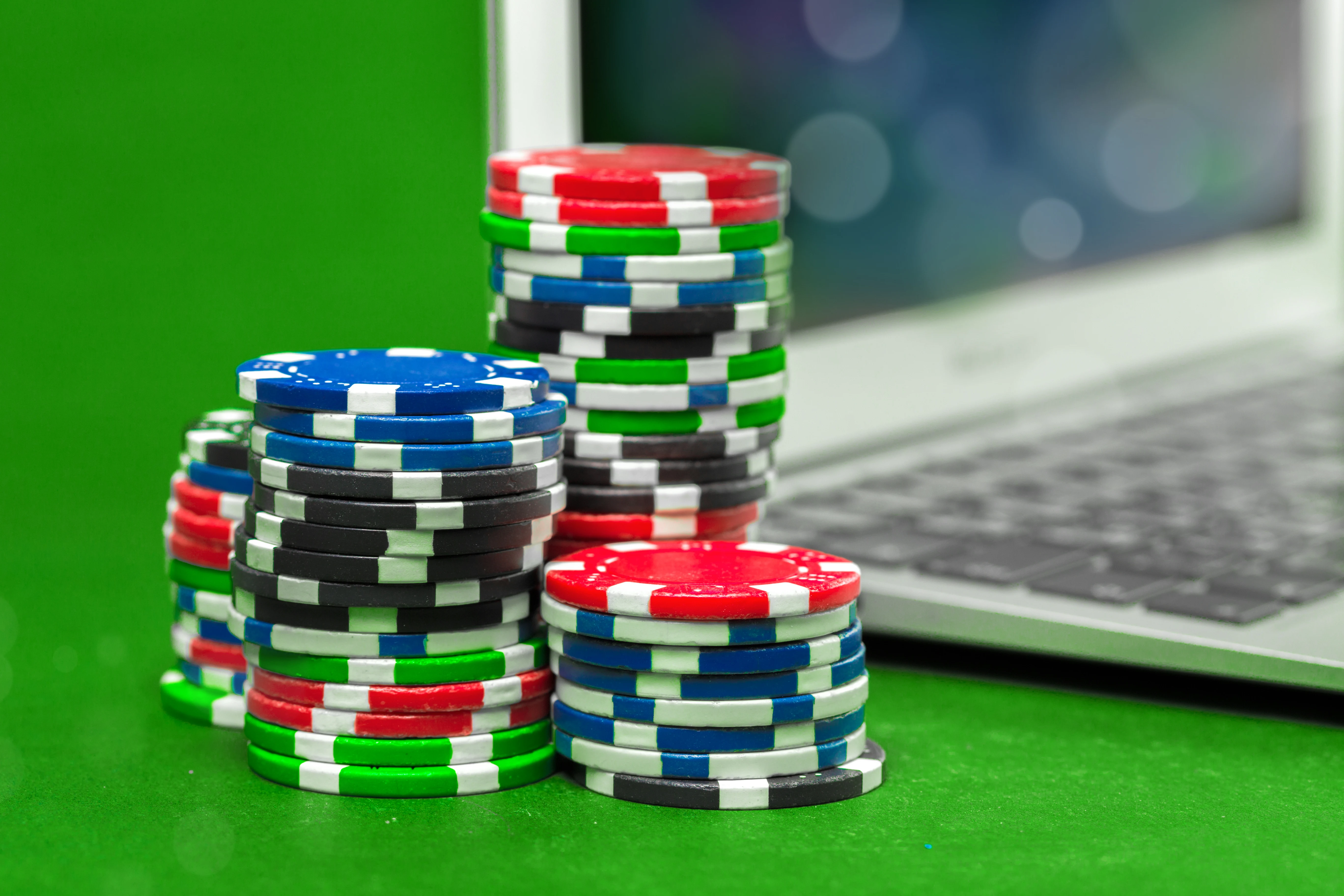 A stack of chips next to a blurred image of Apple Macbook Air on a green casino table