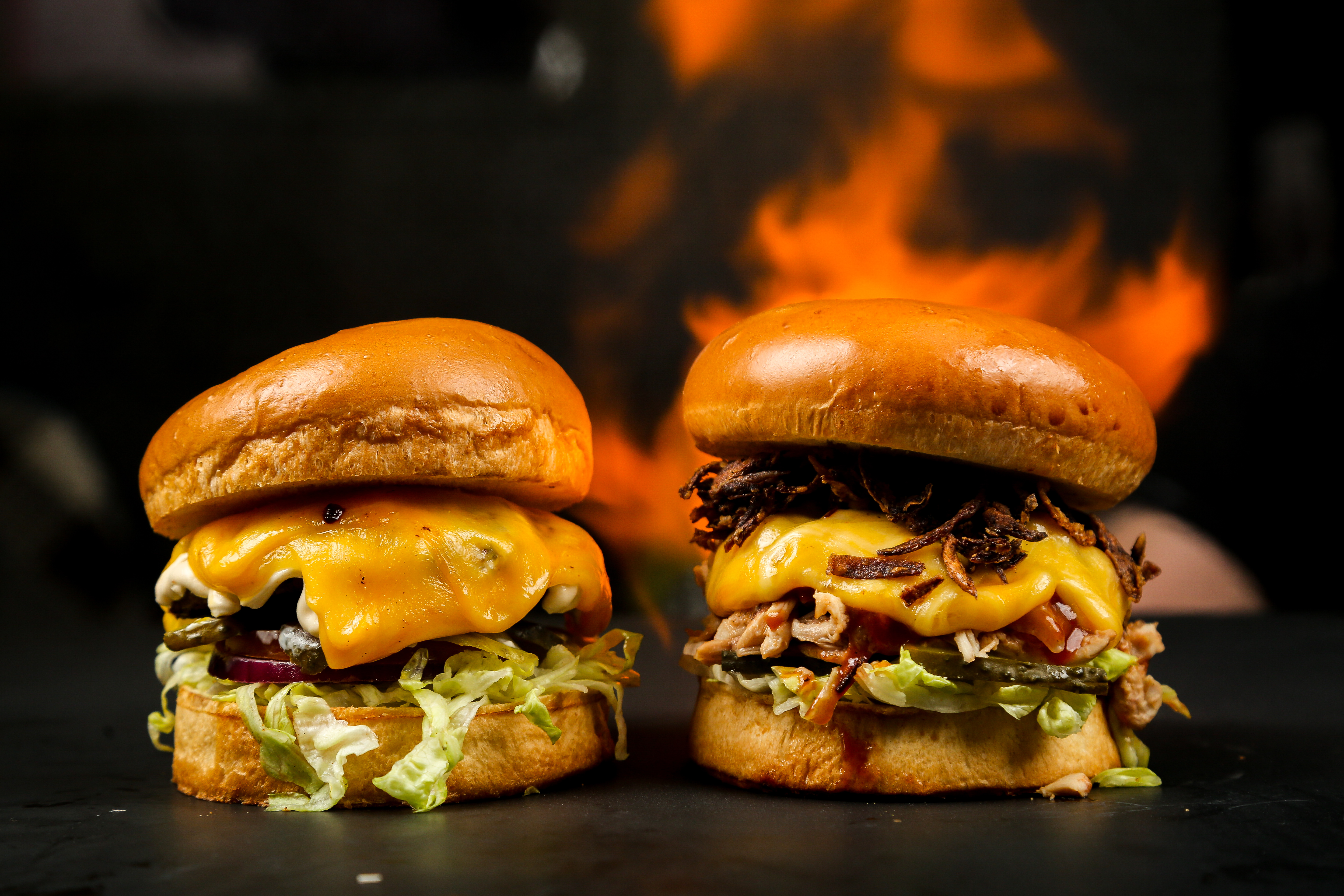 Two cheese burgers on a stand in front of grill with fire