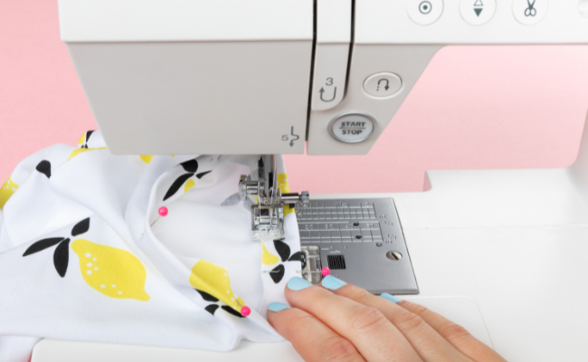 A Tabitha t shirt under the foot of a sewing machine with a hand holding the project in place