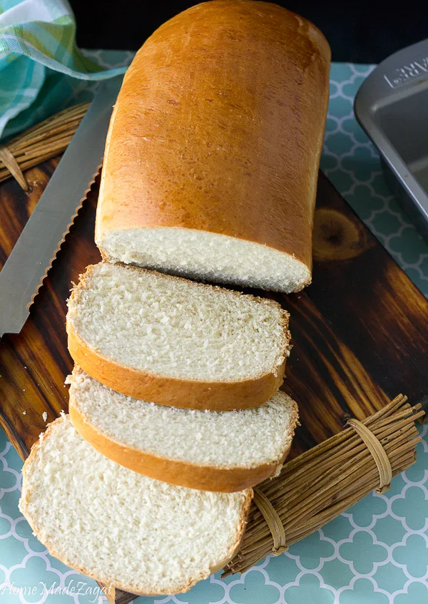 A baked loaf of hard dough bread with some slices on a cutting board.