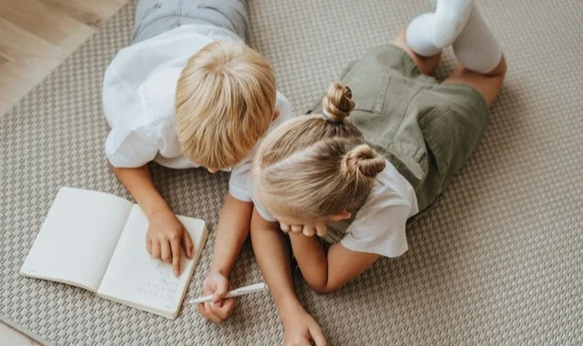طفلان يستلقيان على حصيرة يكتبان في دفتر ملاحظات