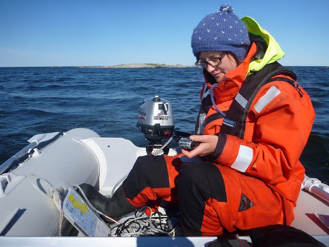 Pelastautumispukuinen henkilö kumiveneessä tuijottaa käsi-GPS-laitetta