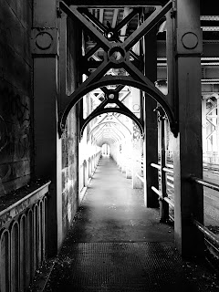 A black and white photograph showing the view along the pedestrian walkway of the High Level Bridge.  There are Victorian looking iron pillars stretching off into the distance.  Photograph by Kevin Nosferatu for The Skulferatu Project.