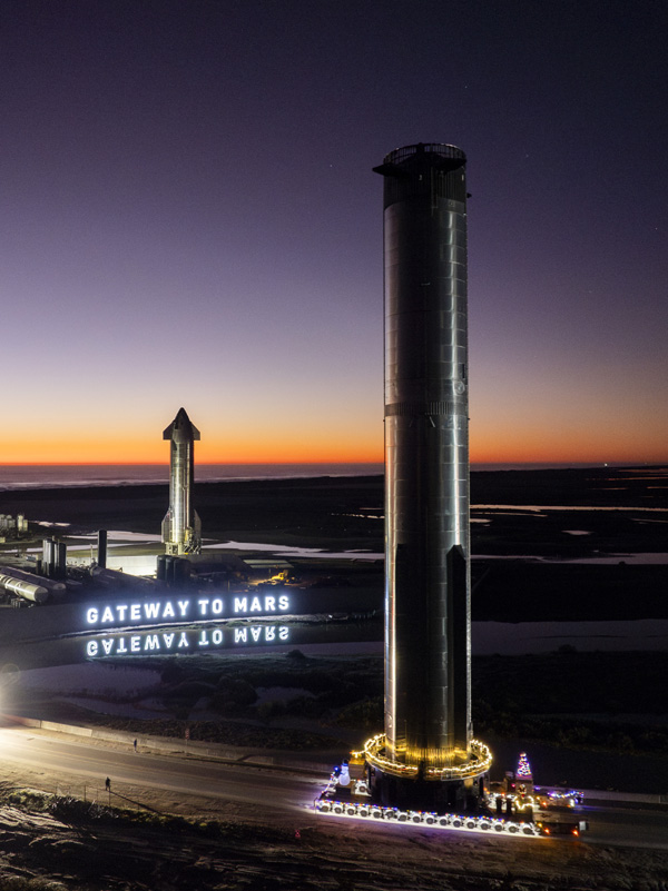 With Ship 28 standing tall nearby, Booster 10 rolls to the Orbital Launch Site at Starbase, Texas...on December 18, 2023.