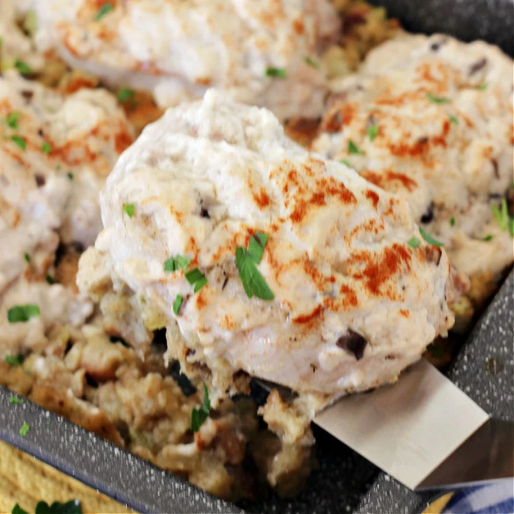 A spatula lifting up a serving of pork chops and stuffing bake over a pan of the ready to eat casserole