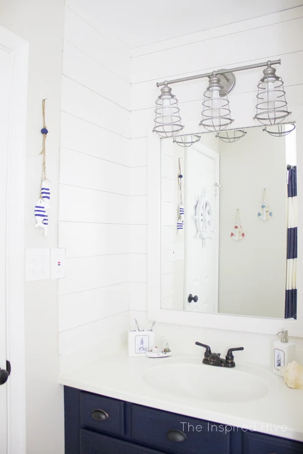 Get the nautical look in your bathroom with a galvanized light, painted cabinets, and nautical accessories.