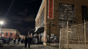 Nighttime view of Franklin Music Hall in Philadelphia with concertgoers arriving for Kraftwerk’s Multimedia Tour 2025. The venue's industrial-style brick exterior and dimly lit urban surroundings set the scene for the legendary electronic music pioneers' performance.