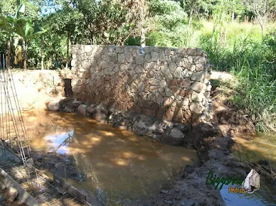 Construção do muro de pedra com pedra bruta para a base da construção da ponte de concreto na entrada da empresa em Atibaia-SP.