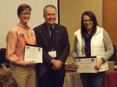 Julie Olson and Patty Martin holding awards. Standing next to Tom Durkin.