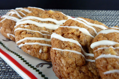 A row of sticky toffee pudding cookies, spiced cookies with dried fruits and drizzled with white chocolate. Photographed on a white plate with a red and green border.