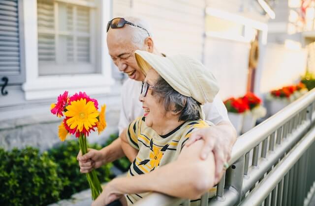 Elderly Asian couple with flowers standing and laughing