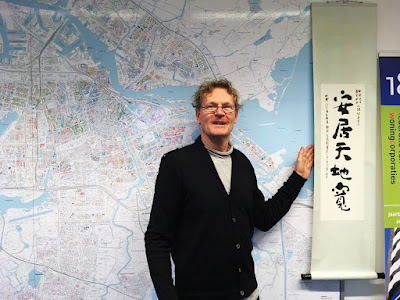 這是Jeroen阿姆斯特丹辦公室的一隅，他站在全市社會住宅地圖前，與住盟贈送的「安居天地寬」(尤俊明老師題字)一起合照。