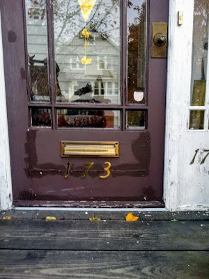 Closeup of the brown front door, with paint in poor condition and the house numbers aged