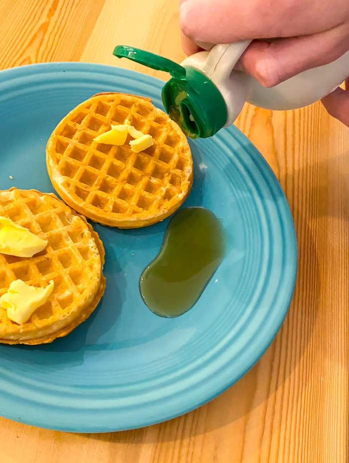Trader Joe's Gluten-Free Toaster Waffles on plate with butter, hand pouring syrup out of bottle