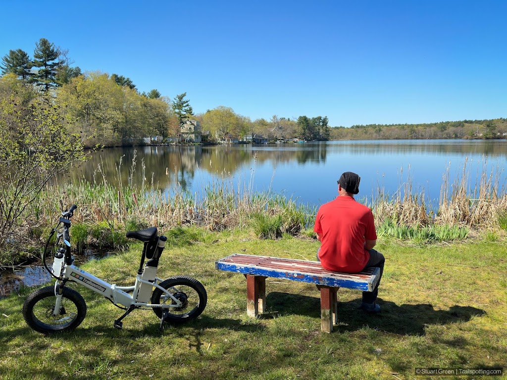 Man sits on a bench looking out over the calm and expansive pond beyond.