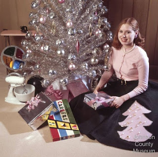 Young woman sitting by an aluminum tree with lots of presents and a color wheel under it.