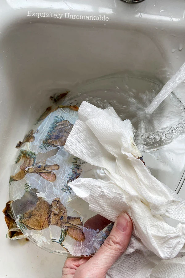 Washing Decoupage napkin off a glass plate with soap and water in a sink