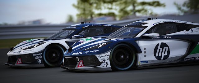 two dark blue and white HP sponsored Corvette C8R photographed from the side with trees behind an Armco barrier in the background