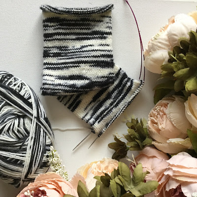 Zebra-striped knitted sock-tube and ball of yarn surrounded by peach flowers