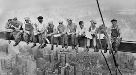 Black and white photo of eleven workers sitting on the steel beam on top of the skyscraper