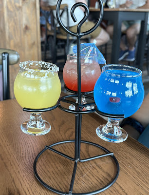 A flight of three different colored cocktails in a metal stand for the Jamaican Me Crazy Flight