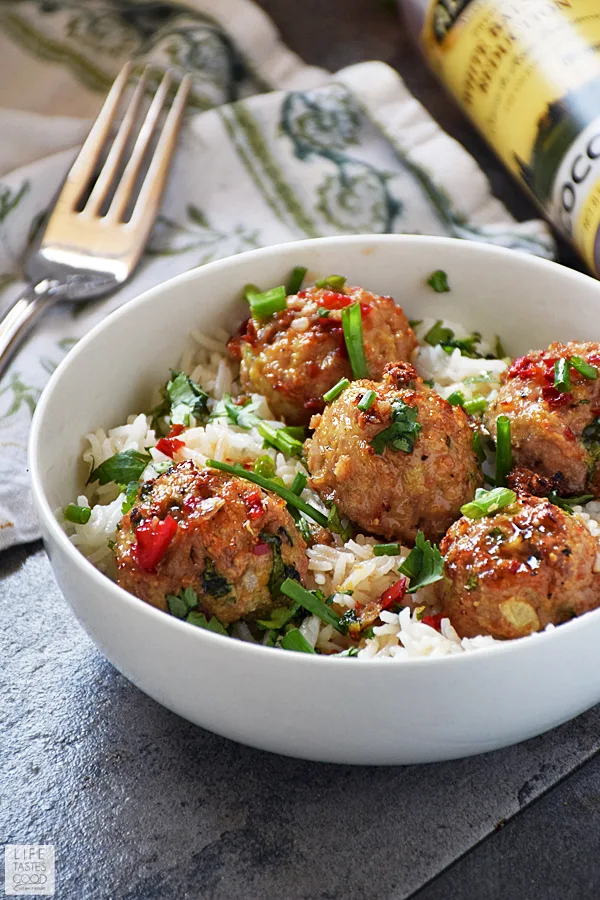 Side view of Asian pork meatballs over creamy coconut rice in a white dinner bowl, garnished with chives.