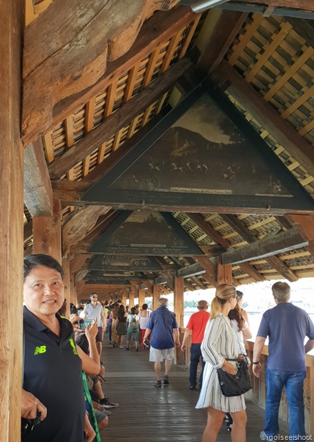 the iconic Chapel Bridge or Kapellbrücke. This is a covered wooden footbridge spanning diagonally across the River Reuss and has an iconic water tower in the middle. A walk on the Chapel Bridge at Luzern.