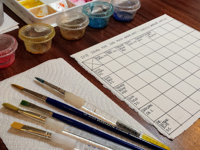 Workspace is arranged for mixing to begin. Brushes to left of watercolor paper.  Pigment in plastic cups arranged in order.