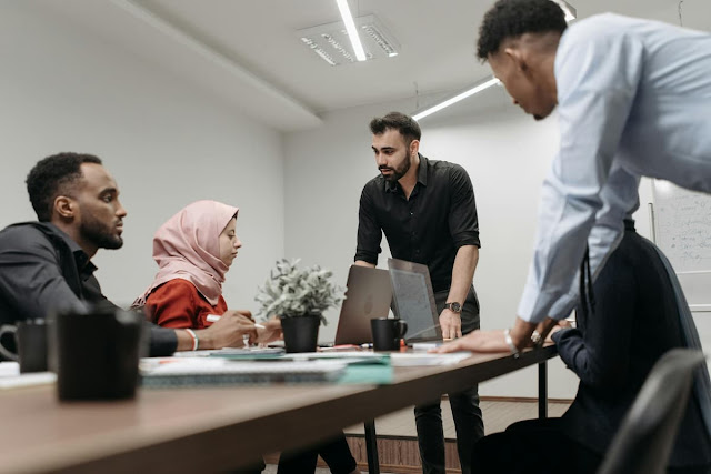 مجموعة متنوعة من المهنيين، رجال ونساء، مجتمعون حول طاولة مؤتمرات مع حواسيب محمولة مفتوحة، يناقشون استراتيجيات الاستثمار العقاري في السعودية.