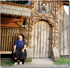 old lady in front of traditional village style wooden gate