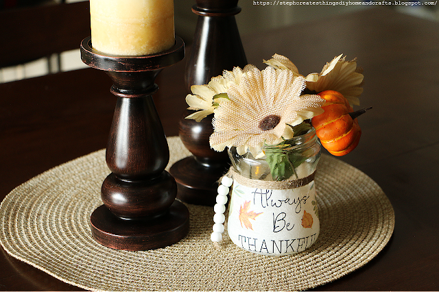 Glass jar decorated with fall napkin and displaying faux floral and craft pumpkin