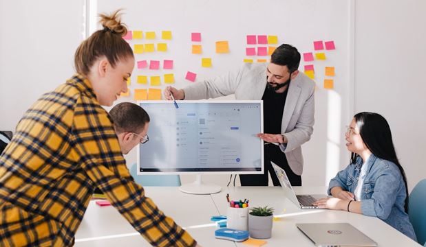 Business meeting where one businessman is discussing examples of sales analytics and pointing at a screen